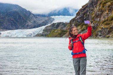 Tourist woman taking selfie photo at Mendenhall glacier in Juneau, Alaska. Famous tourism destination on Alaska cruise, USA travel clipart