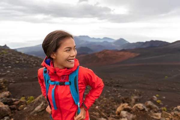 Senderismo Mujer asiática en el paisaje de volcanes al aire libre caminando en Hawaii. Caminante feliz en caminata con mochila y chaqueta de lluvia roja. — Foto de Stock