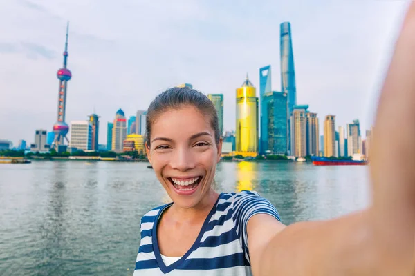 Selfie Asian tourist chinese woman China travel. Smiling young girl excited holding smartphone camera to take a picture with phone of herself in front of Shanghais skyline of skycrapers. — Stock Photo, Image