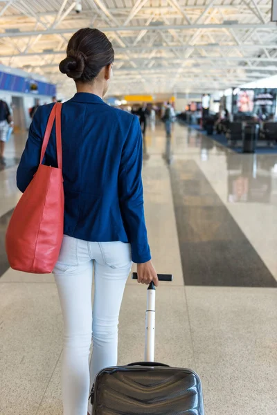 Mujer viajera caminando a través de la terminal del aeropuerto va a puerta que lleva bolso y equipaje de mano de mano de mano para viajar en avión —  Fotos de Stock