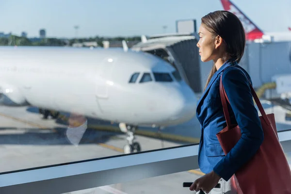 Havaalanındaki pencereye bakan kadın. Asyalı turist kalkıştan önce yolcu kapısında beklerken uçaklara bakarak rahatlıyor. Seyahat yaşam tarzı — Stok fotoğraf