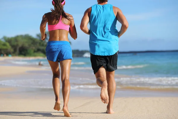 Zwei Läuferpaare laufen gemeinsam am Strand. Menschen von hinten joggen barfuß auf Sand an tropischen Reisezielen davon. Unterkörper, Beine, Füße — Stockfoto