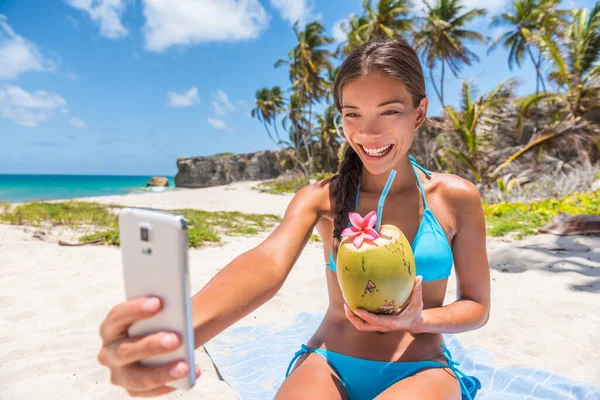 Ευτυχισμένο κορίτσι που βγάζει selfie στις καλοκαιρινές διακοπές στην παραλία. Χαριτωμένο ασιατικό πολυφυλετικό μπικίνι γυναίκα πίνοντας φρέσκο νερό καρύδας χαμογελώντας κρατώντας το κινητό τηλέφωνο για αυτο-πορτρέτο εικόνα για τροπικά ταξίδια — Φωτογραφία Αρχείου