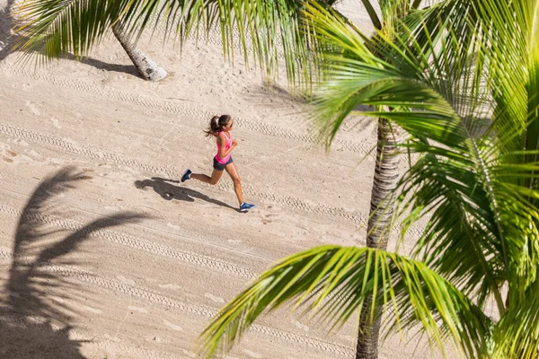 Fitness atlet běží tréninkové kardio na pláži. Žena, která běhá mezi palmami. Pohled shora ze země a písku. Zdravotní a sportovní koncept. Copyspace — Stock fotografie