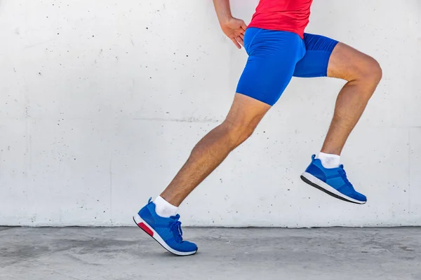 Atleta de fitness hombre corriendo en la acera de asfalto en la calle de la ciudad. Estilo de vida deportivo. Primer plano de las piernas de los corredores inferiores del cuerpo en la carrera de maratón de entrenamiento contra el fondo blanco de la pared. Zapatos, ropa de compresión. —  Fotos de Stock