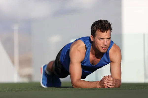 Crossfit Trainingsman gör plank core motion och tränar sina mellersta musklerna. Passa manliga fitness instruktör planking träning utomhus i sommar park gräs. Friluftsstadion. — Stockfoto