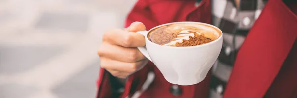 Latte art woman holding drinking at outdoor cafe. Coffee shop city lifestyle banner panorama closeup of hand holding cappuccino cup. — Stock Photo, Image