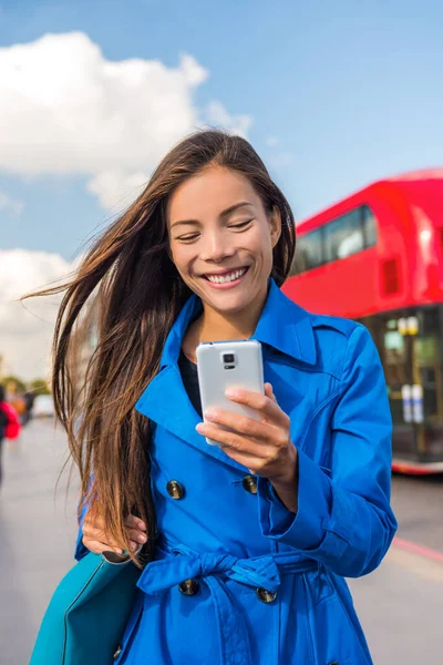 Mujer asiática usando teléfono caminando en la ciudad de Londres estilo de vida urbano. Retrato de mujer de negocios sonriendo feliz sosteniendo el teléfono celular en otoño al aire libre usando gabardina azul — Foto de Stock