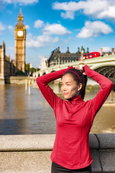 Londense vrouw strikken haar in paardenstaart klaar voor de herfst run. Mooie Aziatische jonge volwassene hechten haar lange bruine haar op outdoor running workout op Westminster brug, Londen Big Ben, UK — Stockfoto