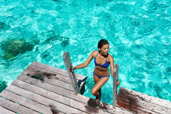 Luxe resort bikini vrouw zwemmen uit het water na het zwemmen op overwater bungalow terras in high-end hotel. Sexy aziatisch meisje in badmode met gebruinde lichaam — Stockfoto