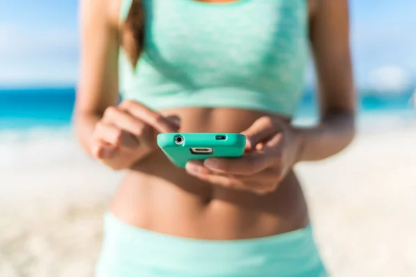 Atleta utilizando la aplicación de fitness smartphone playa entrenamiento —  Fotos de Stock