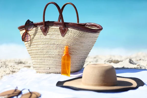 Donna accessori da spiaggia sulla sabbia per il concetto di vacanza estiva. Borsa di paglia, cappello da sole e crema solare lozione o abbronzatura bottiglia spray olio con fondo blu oceano per le vacanze di viaggio. — Foto Stock