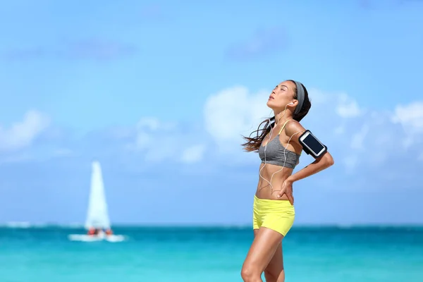 Moe van het joggen vrouw vangt haar adem het nemen van een pauze van harde training. jong aziatische vrouwelijke atleet loper houden haar rug in pijn na intense cardio lopen oefening op lange strand run. — Stockfoto