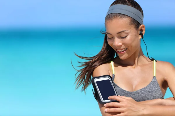 Fit woman using smartphone fitness app on armband. Young Asian female runner touching the display touchscreen on sports arm strap with mobile phone for listening to music or as activity tracker. — Stock Photo, Image