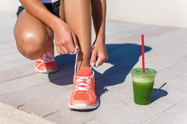 Corrente atleta corridore donna prepararsi per la mattina sulla spiaggia gestito legando lacci scarpa di scarpe da corsa con colazione frullato vegetale verde. Primo piano a piedi. Fitness e stile di vita sano concetto — Foto Stock