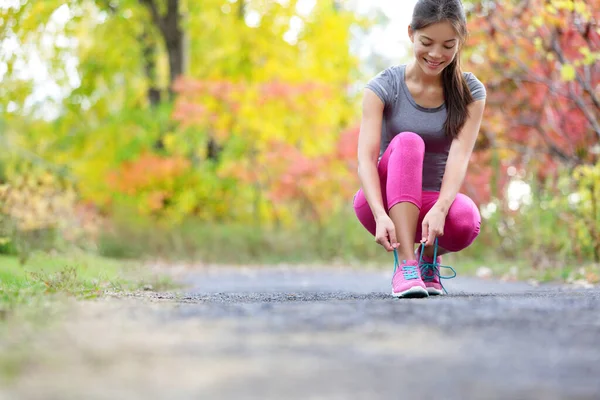 Бегающая женщина в туфлях завязывает шнурки для бега. Крупный план девушки, готовящейся к пробежке шнурками для спортивной обуви. Female sport runner outdoors on forest path in spring fall season. — стоковое фото