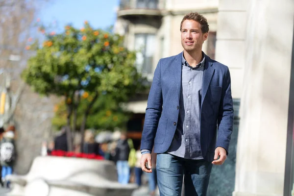 Guapo joven hombre de negocios caminando por la calle de la ciudad por la mañana va a trabajar en la oficina llevar traje casual inteligente de traje de lana y vaqueros azules. Estilo de vida urbano de jóvenes profesionales. Hombre caucásico. — Foto de Stock