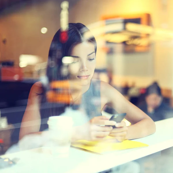 Café mujer estilo de vida de la ciudad en el teléfono beber mensajes de texto de café en la aplicación de teléfono inteligente sentado en interiores en la cafetería urbana de moda. fresco joven moderno mezclado raza asiático caucásico modelo femenino en su 20s. — Foto de Stock