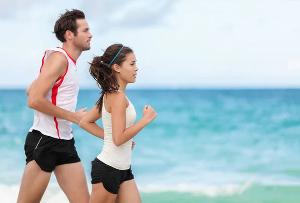 Fitness interracial par löpare körs på stranden. Löpande par joggar tillsammans utanför på havet bakgrund. Idrottare tränar cardio utomhus träna. — Stockfoto