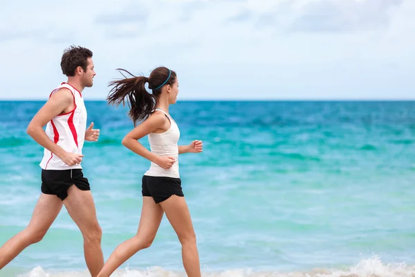 Fitness interracial par löpare körs på stranden. Löpande par joggar tillsammans utanför på havet bakgrund. Idrottare tränar kondition utomhus träna. Passar asiatisk kvinna, vit man. — Stockfoto