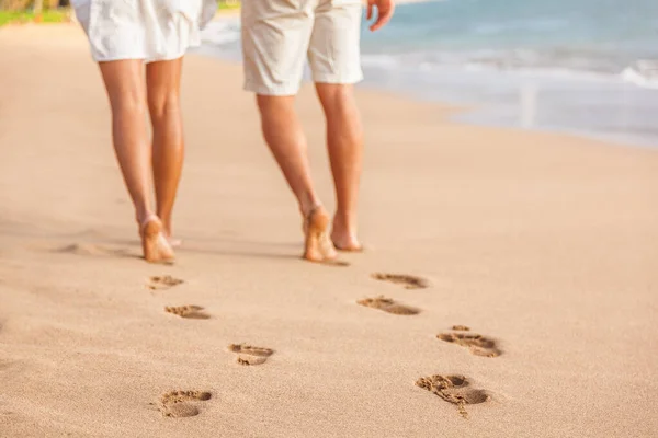 Para na plaży relaksująca się o zachodzie słońca na bosaka. Skup się na śladach stóp w złotym piasku. Zbliżenie nóg. Romantyczne wakacje na plaży. Młodzi ludzie od tyłu odchodzą ku szczęściu. — Zdjęcie stockowe