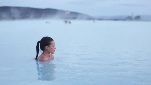Piscine thermale - femme relaxante dans un spa géothermique en Islande. Fille appréciant se baigner dans un lagon d'eau bleue attraction touristique islandaise. Portrait de la race mixte asiatique modèle féminin caucasien au coucher du soleil. — Video