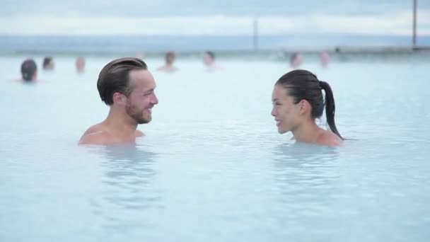 Geothermische kuuroord. Jong stel ontspant zich in het warmwaterbronnen zwembad in IJsland. mensen die genieten van het zwemmen in een blauwe lagune IJslandse toeristische attractie — Stockvideo
