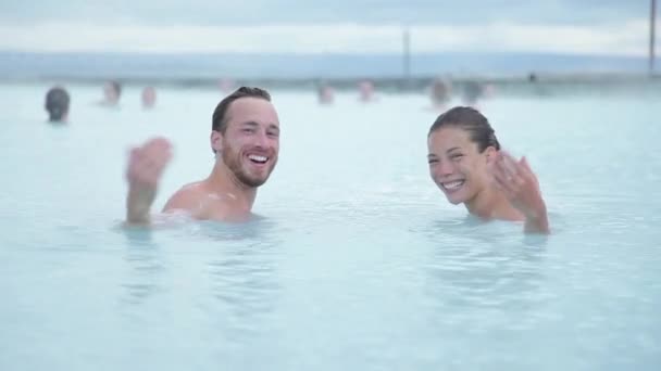 IJsland reist. Warmwaterbron geothermische spa. Een paar nodigen je uit om met hun zwaaiende hand te verwelkomen. Romantisch koppel in liefde ontspannen in warm zwembad op IJsland — Stockvideo