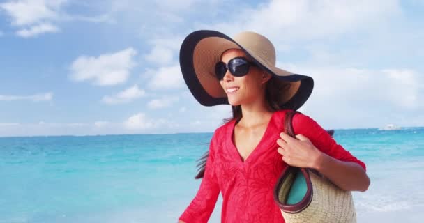 Πολυτελείς διακοπές στην παραλία κομψή κυρία περπάτημα στην παραλία βόλτα με beachwear καπέλο ήλιο και άχυρο tote τσάντα φορώντας κόκκινο φόρεμα συγκάλυψης. SLOW MOTION VIDEO — Αρχείο Βίντεο