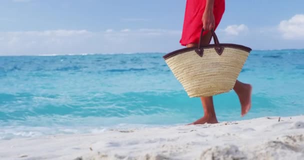 Kobieta spacerująca po tropikalnych letnich wakacjach w czerwonej sukience trzymająca torbę plażową relaksującą podczas wakacji. Dolna połowa, nogi i stopy nierozpoznawalnej młodej damy w luksusowych strojach plażowych. SŁUGA MOTION — Wideo stockowe