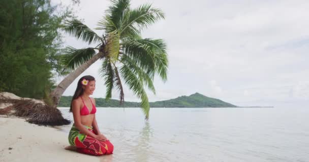 Vídeo muy icónico de una mujer vestida con pareo tradicional y Bikini relajándose sentada en una playa paradisíaca en Bora Bora. Polinesia Francesa Beach Vacation Travel. Chica feliz en Tahití — Vídeo de stock