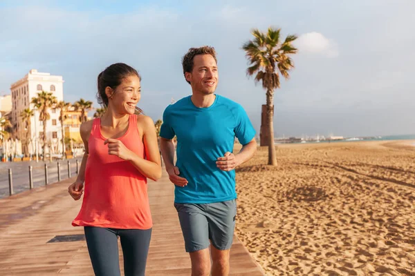 Pareja corriendo corriendo en Barcelona Beach, Barceloneta. Estilo de vida saludable gente corredores entrenando fuera en el paseo marítimo. Pareja multirracial, Mujer asiática, Hombre de fitness caucásico haciendo ejercicio, España — Foto de Stock