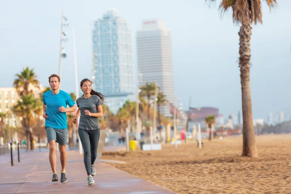 Running man and woman couple jogging on Barcelona Beach, Barceloneta. Healthy lifestyle people runners training outside on boardwalk. Multiracial couple, Asian woman Caucasian fitness man working out — Stock Photo, Image