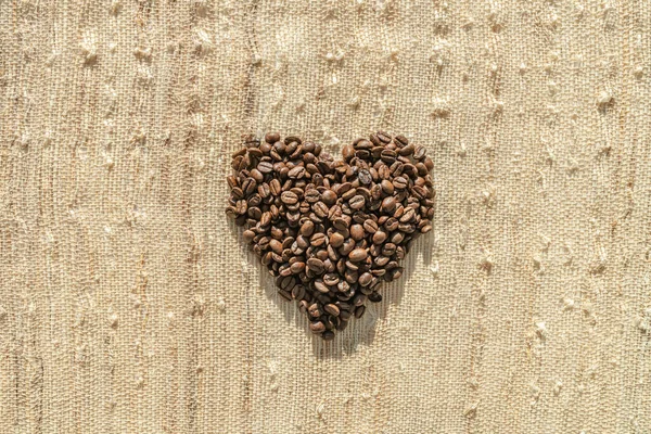 Coffee beans top flat view of heart shaped cafe background coffee lover concept on rustic bag texture — Stock Photo, Image
