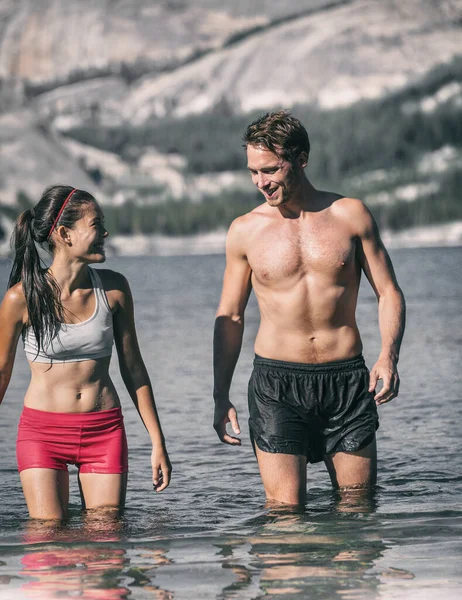 Yüzen bir çift yüzücü soğuk su gölünde eğleniyor. Açık havada kutup dalışı yarışması için. Spor kıyafetleri içinde gülen Asyalı kadın ve dondurucu sıcaktan çıkan genç adam. — Stok fotoğraf