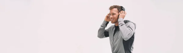 Hombre escuchando música usando auriculares poniéndolos mientras camina sobre fondo de cabecera de pared blanca para gimnasio de fitness o atleta deportivo estilo de vida saludable en casa utilizando tecnología portátil al aire libre — Foto de Stock