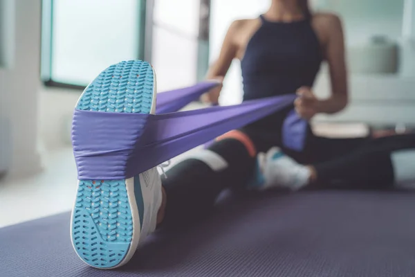 Ejercicio de banda de resistencia en casa. Mujer haciendo ejercicios de pilates usando correa elástica tirando con los brazos para el entrenamiento de hombros en estera de yoga en interiores —  Fotos de Stock