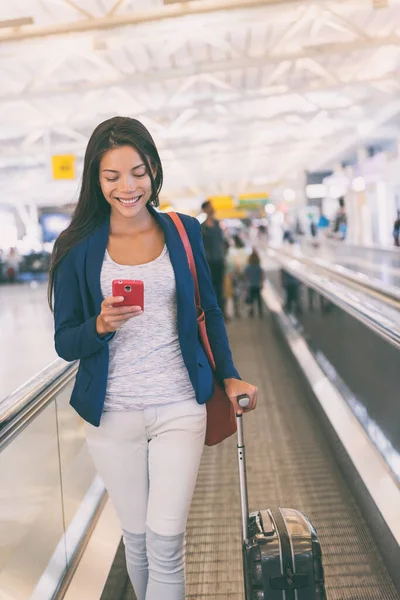 Viaggio aeroporto donna asiatica utilizzando il telefono cellulare a piedi con valigia in movimento passerella nel terminale in viaggio d'affari. Tecnologia wifi online in lounge. Stile di vita dei viaggi aerei — Foto Stock