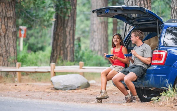 Viagem de estrada casal turista comer comida almoço na parte de trás do carro no verão camping viagem de férias. Pessoas de condução felizes — Fotografia de Stock