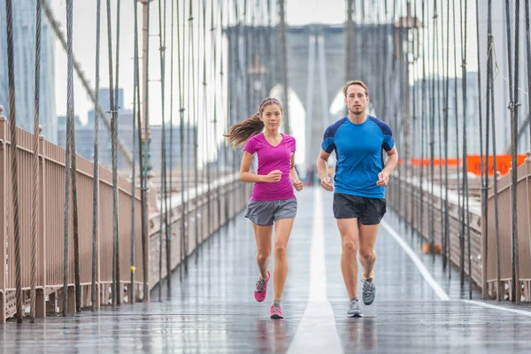 New York City koşucuları Brooklyn Köprüsü 'nde maraton koşusu için antrenman yapıyor. Açık havada yağmurlu bir günde koşan etkin ırklar arası bir çift. Yaz yağmuru. Asyalı kadın, beyaz adam. - Stok İmaj