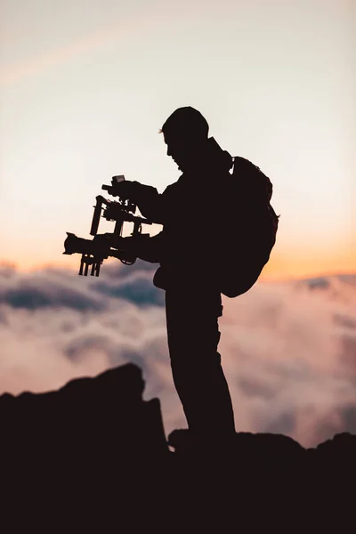 Videografo uomo riprese filmati utilizzando telecamera dlsr montata su attrezzature stabilizzatore gimbal. Video troupe di produzione per film, cinema. Silhouette di regista professionista riprese all'aperto — Foto Stock