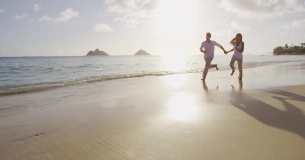 Διακοπές ζευγάρι στην παραλία στο ηλιοβασίλεμα ρομαντικό κρατώντας τα χέρια τρέχει παιχνιδιάρικο — Αρχείο Βίντεο