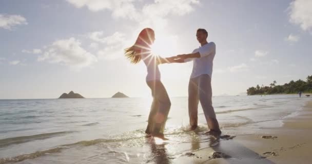 Романтическая пара, гуляющая по пляжу на закате, танцующая вокруг, держась за руки — стоковое видео