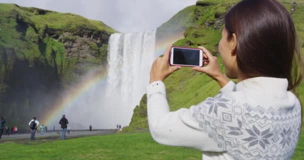 Mulher turista por cachoeira Skogafoss na Islândia tirar foto com telefone — Vídeo de Stock