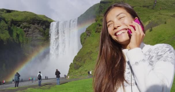 Vrouw toerist door waterval Skogafoss op IJsland te praten over de telefoon — Stockvideo