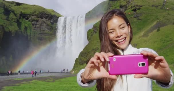 Mulher turista por cachoeira Skogafoss na Islândia tirar foto selfie com telefone — Vídeo de Stock