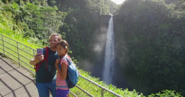 Néhány turista önarcképet készít kamerás telefonnal Hawaiin, Nagy-szigeteken, Akaka Fallsban. Boldog, vidám fiatal multikulturális pár az utazáson — Stock videók