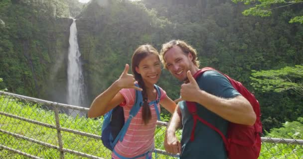 Felices parejas de turistas de pie en sus vacaciones en Hawaii, Big Island, Akaka Falls. Mujer asiática y hombre caucásico mostrando el signo de mano Shaka en el viaje — Vídeos de Stock