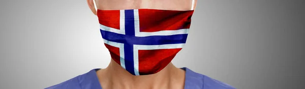 Норвегія маскове друкування прапора на північно-західному лікарському медсанті чоловік або жінка стикаються з PPE на сірому фоновому панорамному прапорі. Концепція Коронавірусу — стокове фото