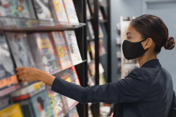 Winkelen binnen tijdens een coronavirus pandemie. Aziatische vrouw draagt gezichtsmasker terwijl in de openbare bibliotheek of het kopen van lectuur tijdschrift bij kiosk winkel in de luchthaven — Stockfoto